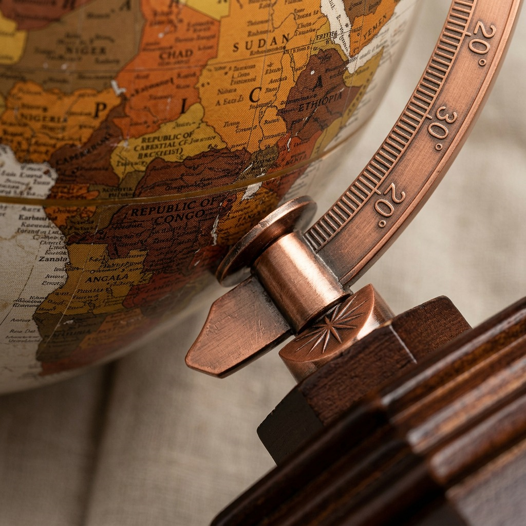 Extreme macro close-up of the antique-style map texture, precise copper meridian details, and wood base on the Randmar Replogle globe.