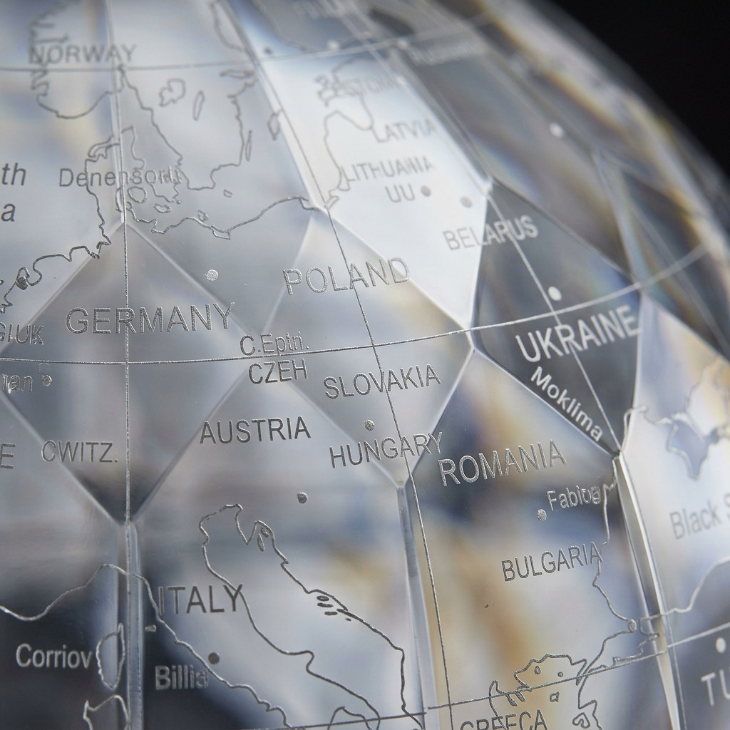 A macro photo focuses on the clear faceted surface and intricate cartography of the CRYSTAL MARQUISE globe.